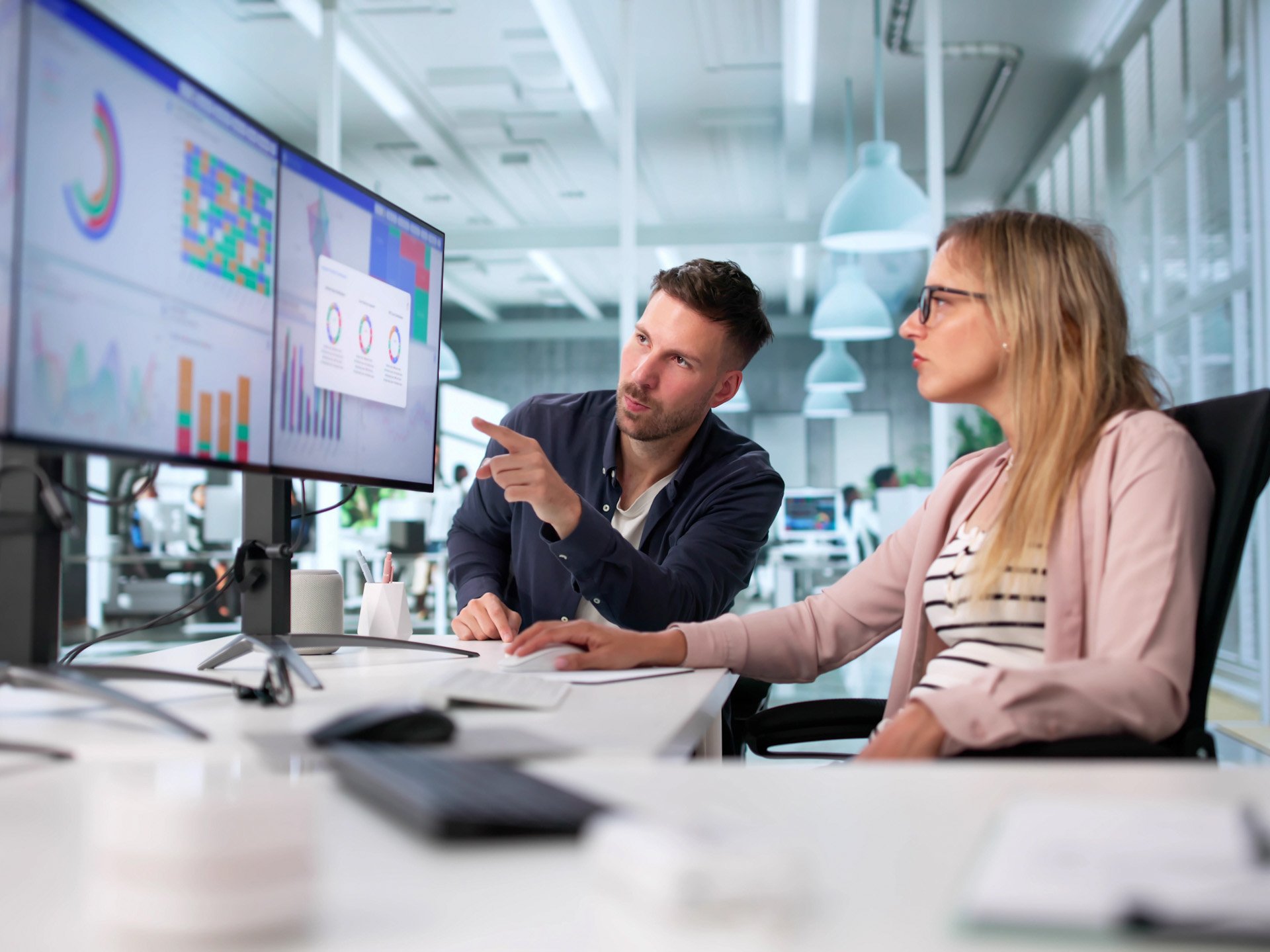 A man and a woman analyze data in front of two monitors